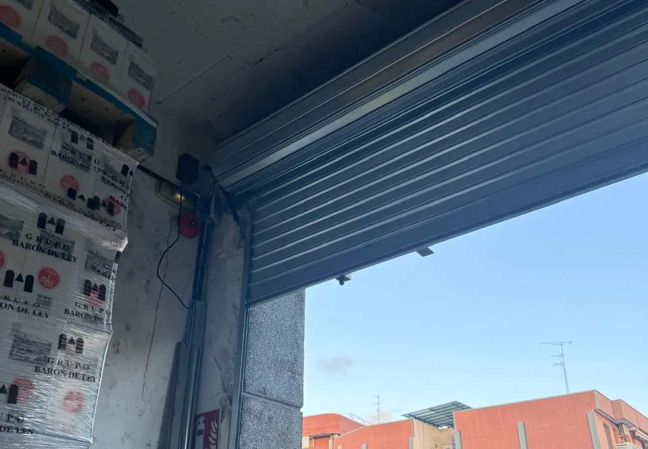 Cierre enrollable metálico recién instalado y a media altura en el acceso de un almacén